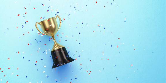 Photo: A small gold trophy with a black base lies on a light blue background, surrounded by red, white, and blue confetti.