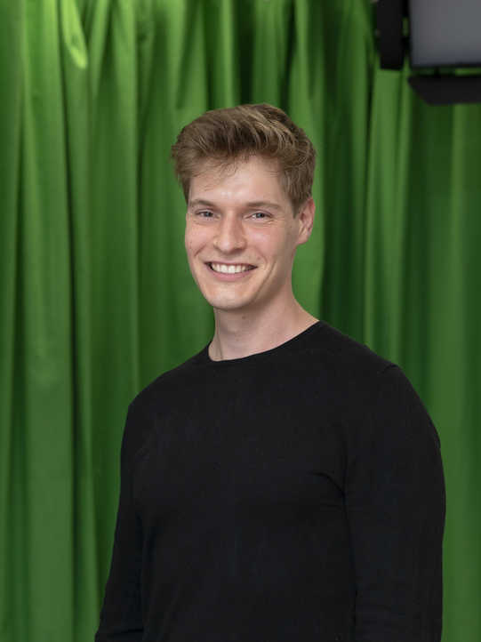 Photo: Profile picture of Tobias Schmidt. He is wearing a black pullover and has short blond hair. Background: green screen.