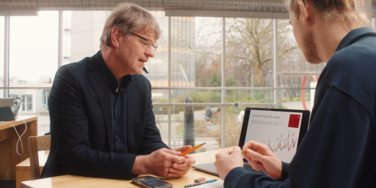 Photo: Prof. Müller and male student are sitting at a desk looking at data on a laptop, which is standing between them