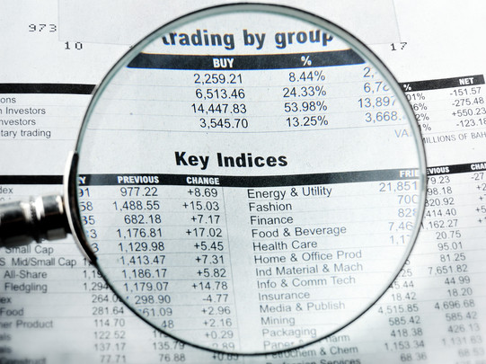 Photo: A magnifying glass focuses on stock market data on a newspaper page.