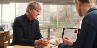 Photo: Prof. Müller and male student are sitting at a desk looking at data on a laptop, which is standing between them