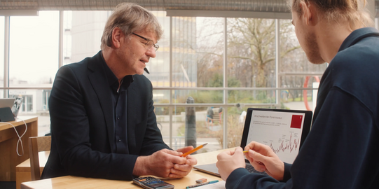 Photo: Prof. Müller and male student are sitting at a desk looking at data on a laptop, which is standing between them