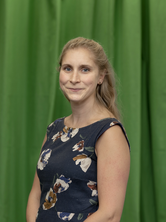 Photo: Profile picture of Lena Marie Hufnagel. She is wearing a dark blue dress with with large floral print and has shoulder-long blond hair. Background: green-screen.