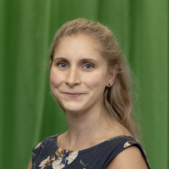 Photo: Profile picture of Lena Marie Hufnagel. She is wearing a dark blue dress with with large floral print and has shoulder-long blond hair. Background: green-screen.
