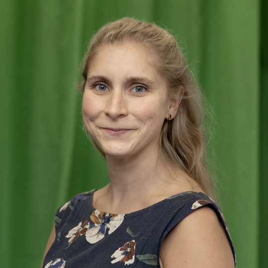 Photo: Profile picture of Lena Marie Hufnagel. She is wearing a dark blue dress with with large floral print and has shoulder-long blond hair. Background: green-screen.