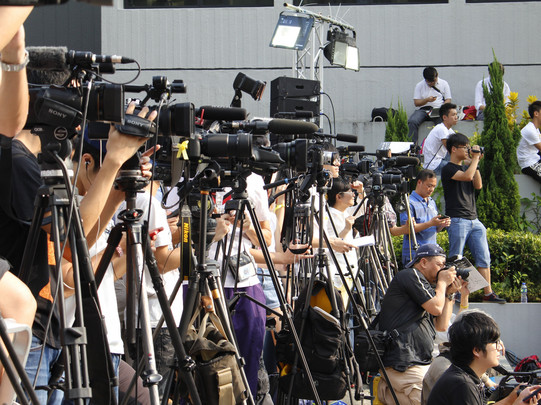 Photo: A large crowd of journalists with TV cameras and microphones are standing outside.