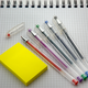 Photo: A set of 5 pencils in different colors are sitting next to a stack of blank yellow post it notes, ready to be used.