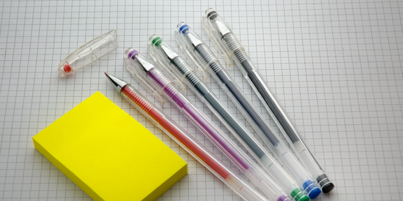 Photo: A set of 5 pencils in different colors are sitting next to a stack of blank yellow post it notes, ready to be used.