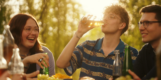 Photo: 3 students are having a cold drink in the late afternoon sun. Background: sun is shining through tree leaves.