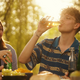 Photo: 3 students are having a cold drink in the late afternoon sun. Background: sun is shining through tree leaves.
