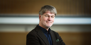 Photo: Profile picture of Prof. Henrik Müller, standing sideways, arms are crossed in front of the chest and head is facing towards the camera.
