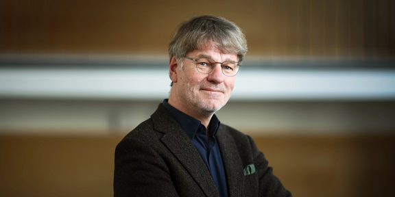 Photo: Profile picture of Prof. Henrik Müller, standing sideways, arms are crossed in front of the chest and head is facing towards the camera.