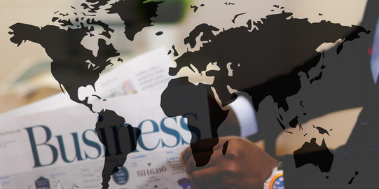 Photo: A map of the world with black shapes of the continents. Background: a business newspaper.