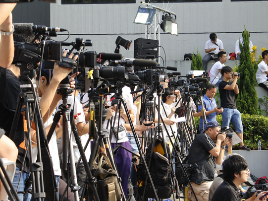 Photo: A large crowd of journalists with TV cameras and microphones are standing outside.