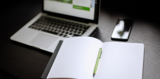 Laptop, notebook and smartphone Photo: A laptop (turned on), an open notebook with pen and a smartphone are lying on a table.