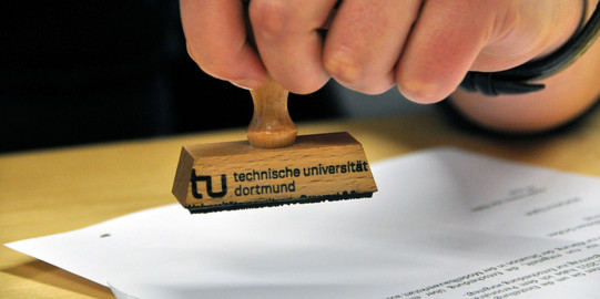Close-up of a hand holding a stamp of TU Dortmund