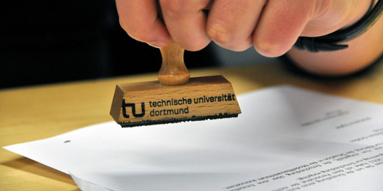 Close-up of a hand holding a stamp of TU Dortmund